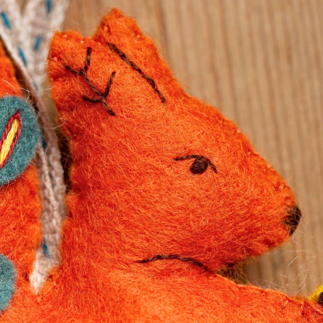 Close-up of the embroidered orange felt squirrel showing its stitched face and ears.