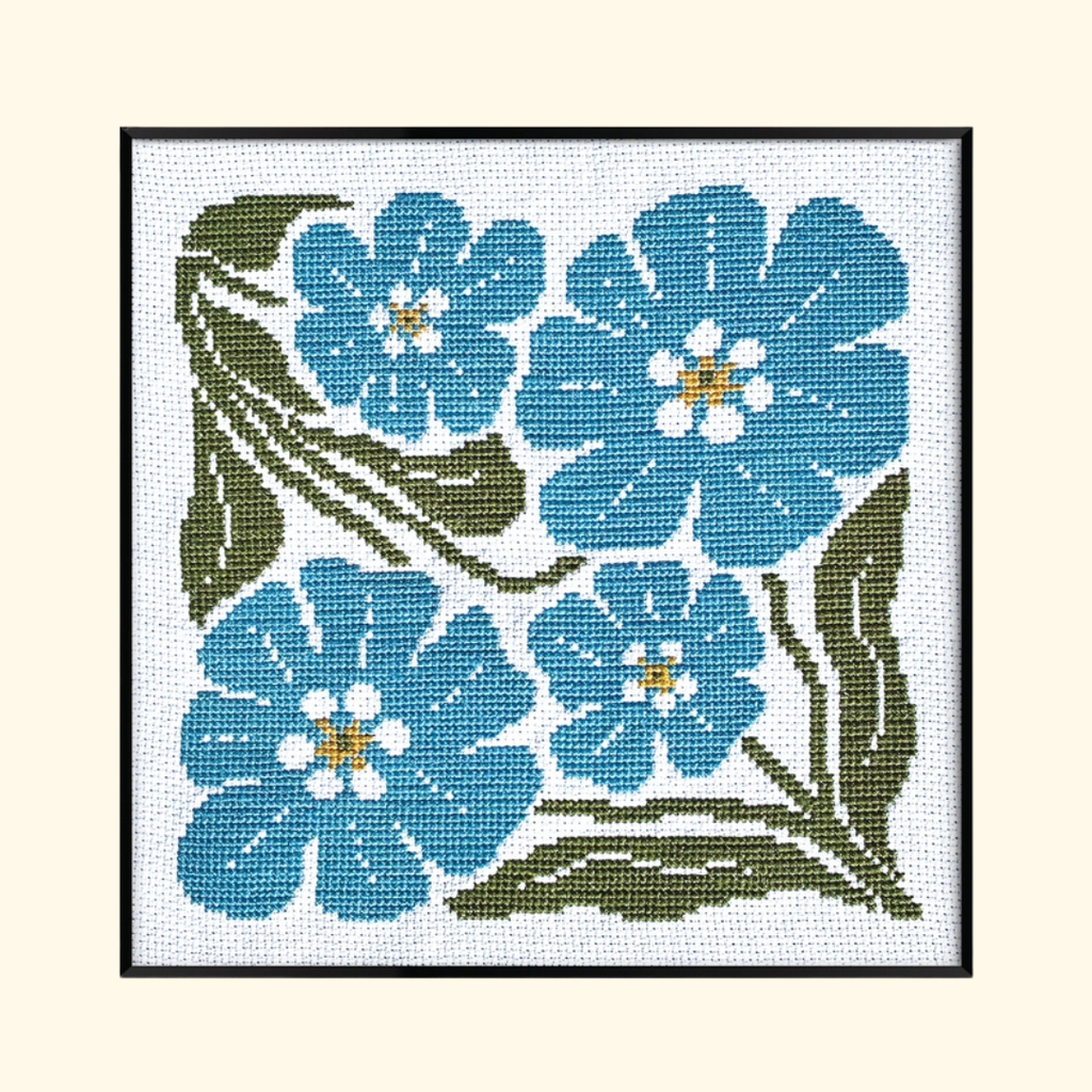 Completed Forget Me Not Grid Cross Stitch Kit by Budgie Goods featuring blue flowers and green leaves in a black frame.