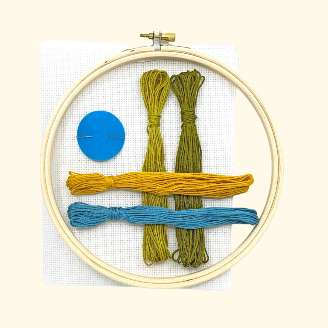 Forget Me Not Grid Cross Stitch Kit by Budgie Goods with embroidery hoop, blue and green threads, white Aida fabric and needle.