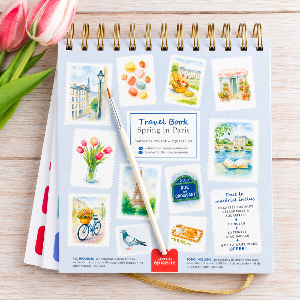 France Watercolour Travel Book by La Petite Epicerie displayed on a wooden table beside pink tulips, featuring colourful French-inspired watercolour illustrations.