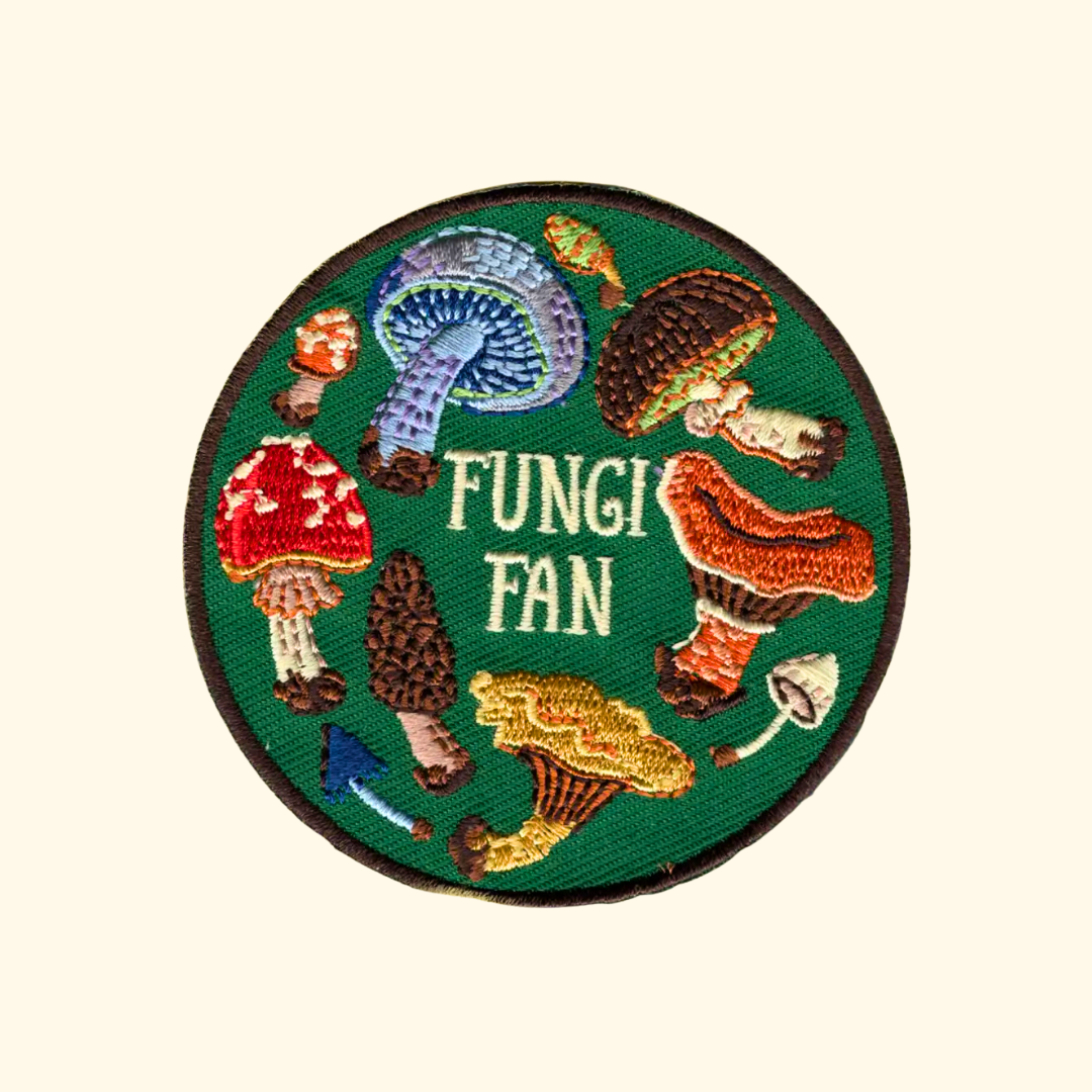 A circular embroidered patch featuring various colorful mushrooms around the words 'FUNGI FAN' in white, set against a light cream background.