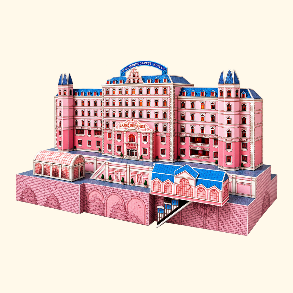 Angled view of the Grand Budapest Hotel paper craft model showing the pink hotel facade, blue rooftop details, balconies and miniature entrance from Wes Anderson's film.