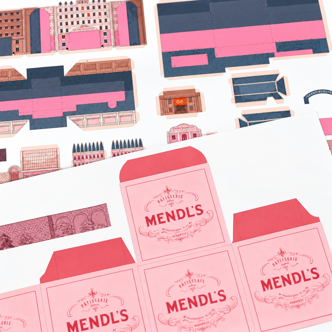 Printed cardstock pieces from the Grand Budapest Hotel paper model kit by Kiko Ilustrador, featuring pink architectural details, windows and miniature Mendl's bakery boxes.