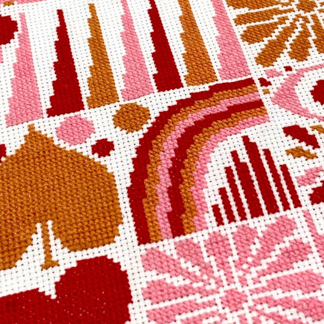 Close up of the Harvest Grid cross stitch showing textured stitches and abstract floral and geometric details in pink, rust and ochre