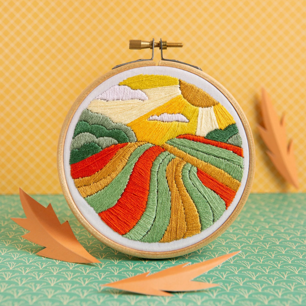 Harvest Time Mini Embroidery Kit by Hawthorn Handmade featuring a vibrant patchwork countryside scene with rolling fields and golden skies.