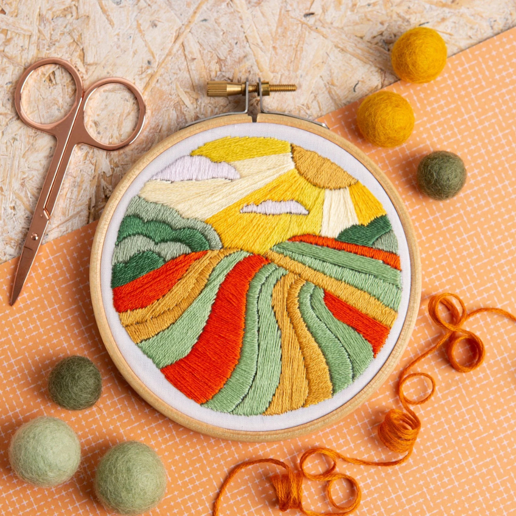 Finished Harvest Time embroidery project displayed in a wooden hoop surrounded by embroidery tools and crafting accessories.