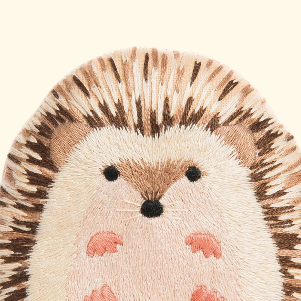 Close-up of the finished Kiriki Press Hedgehog Embroidery Kit, showing the embroidered face, pink hands and feet and detailed brown textured stitching.