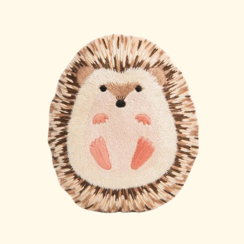 Finished Hedgehog Embroidery Kit by Kiriki Press, featuring a hand embroidered hedgehog doll with textured brown stitching, a cream face and pink hands and feet.