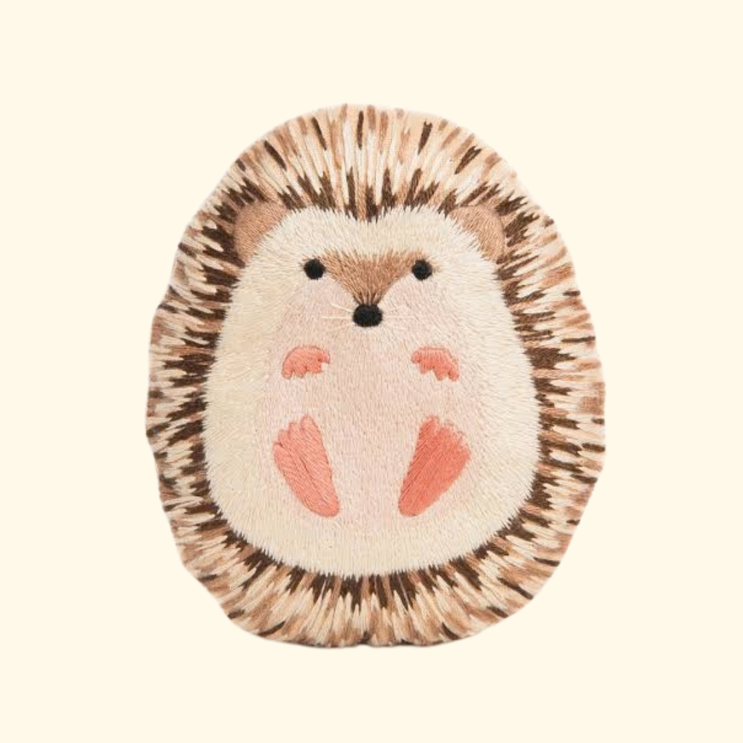Finished Hedgehog Embroidery Kit by Kiriki Press, featuring a hand embroidered hedgehog doll with textured brown stitching, a cream face and pink hands and feet.