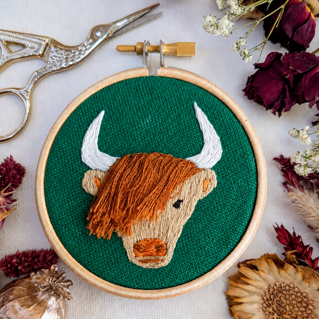Finished Highland cow embroidery displayed with embroidery tools and natural decorations.