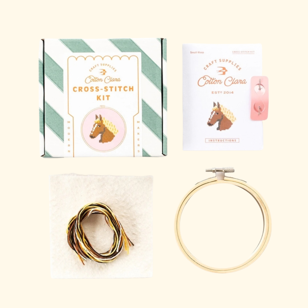 Contents of the Cotton Clara Horse Cross Stitch Kit including bamboo hoop, pink Aida fabric, embroidery threads, needle and instructions.
