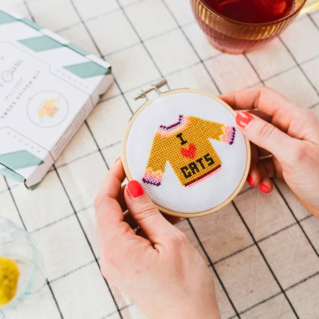 I Love Cats cross stitch being held in a bamboo hoop while stitching, with craft supplies arranged on the table.