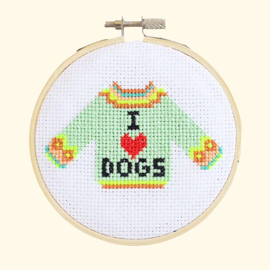 Finished I Love Dogs cross stitch featuring a mint green jumper with colourful details and “I ♥ DOGS” lettering, displayed in a bamboo embroidery hoop.