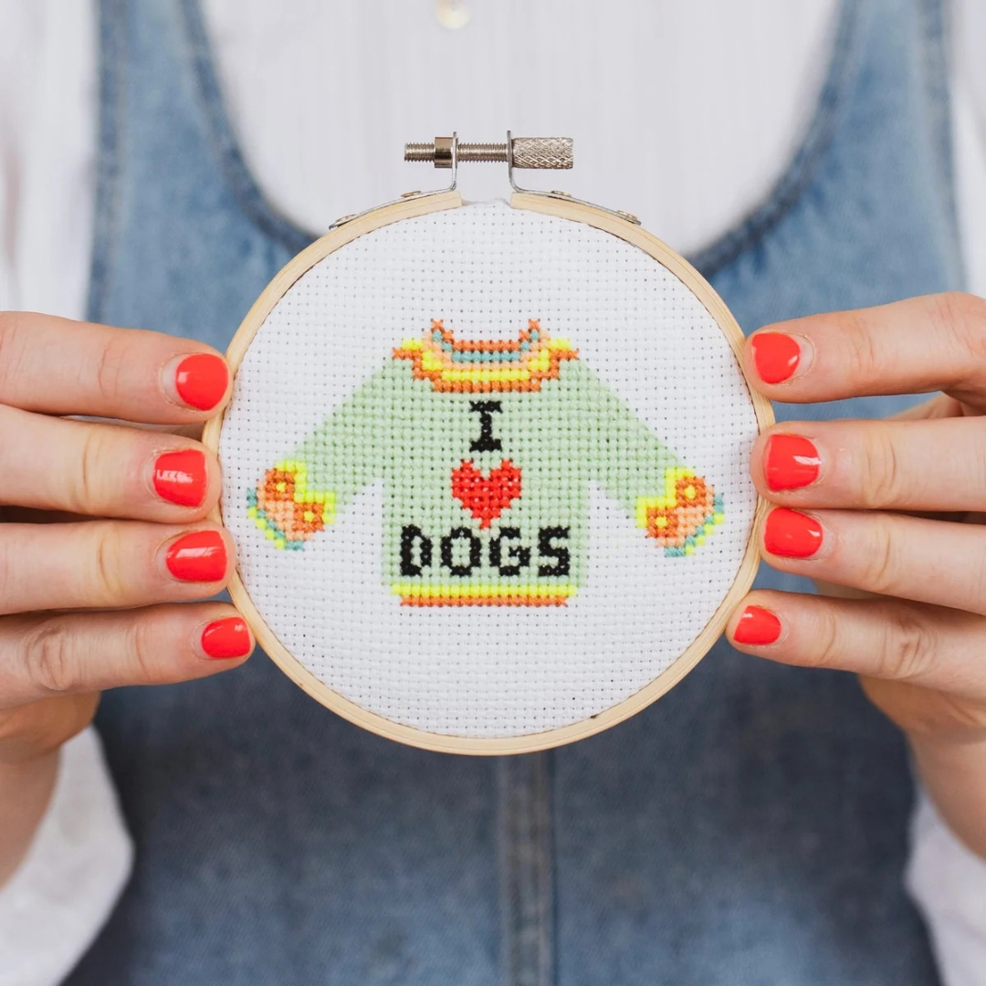 Completed I Love Dogs cross stitch held in a bamboo embroidery hoop, showing the colourful jumper design and lettering.