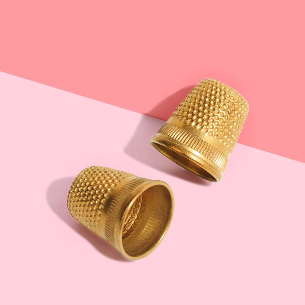 Two gold thimbles on a pink background