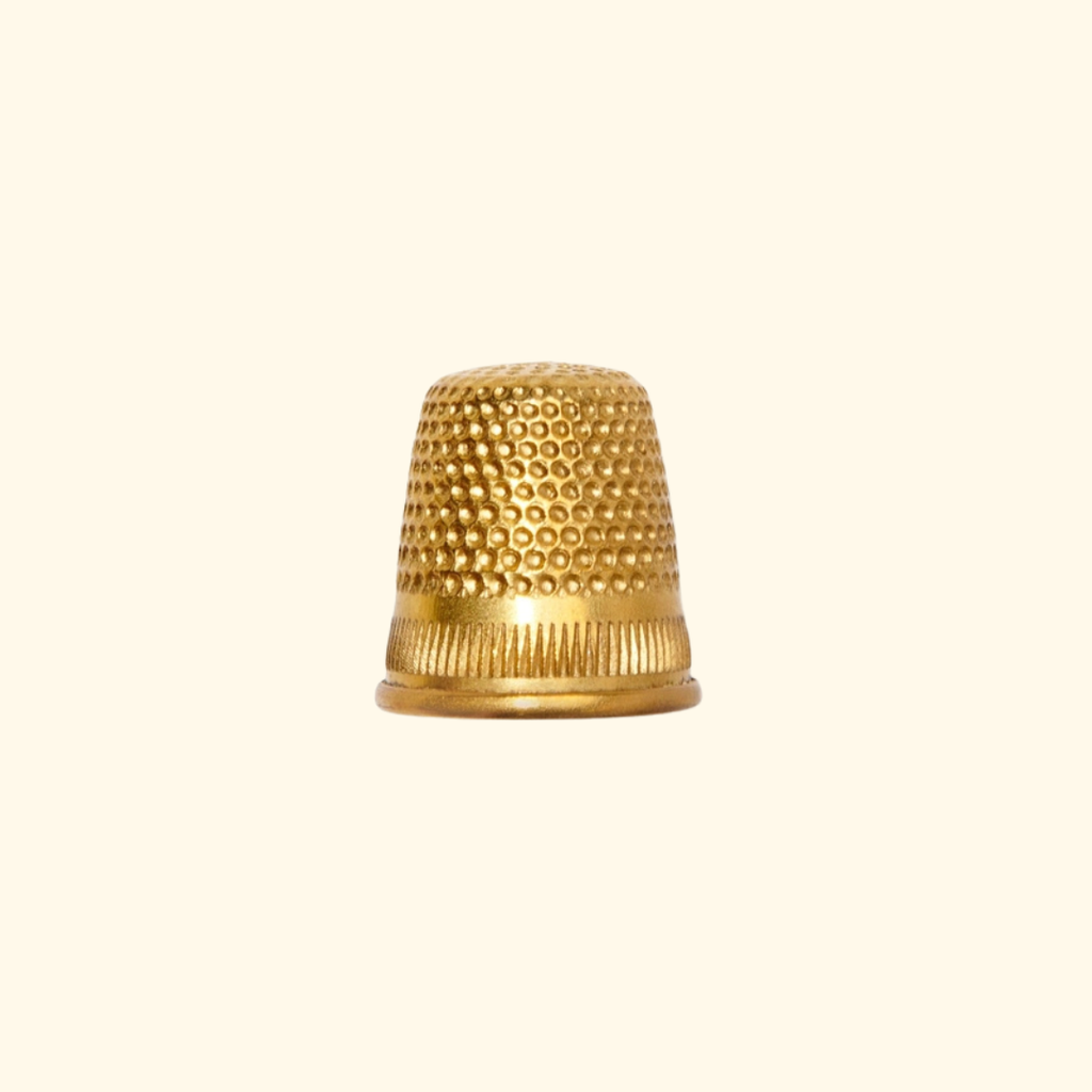 A small metallic gold thimble with a textured beaded top and ribbed base, centered on a plain cream background.