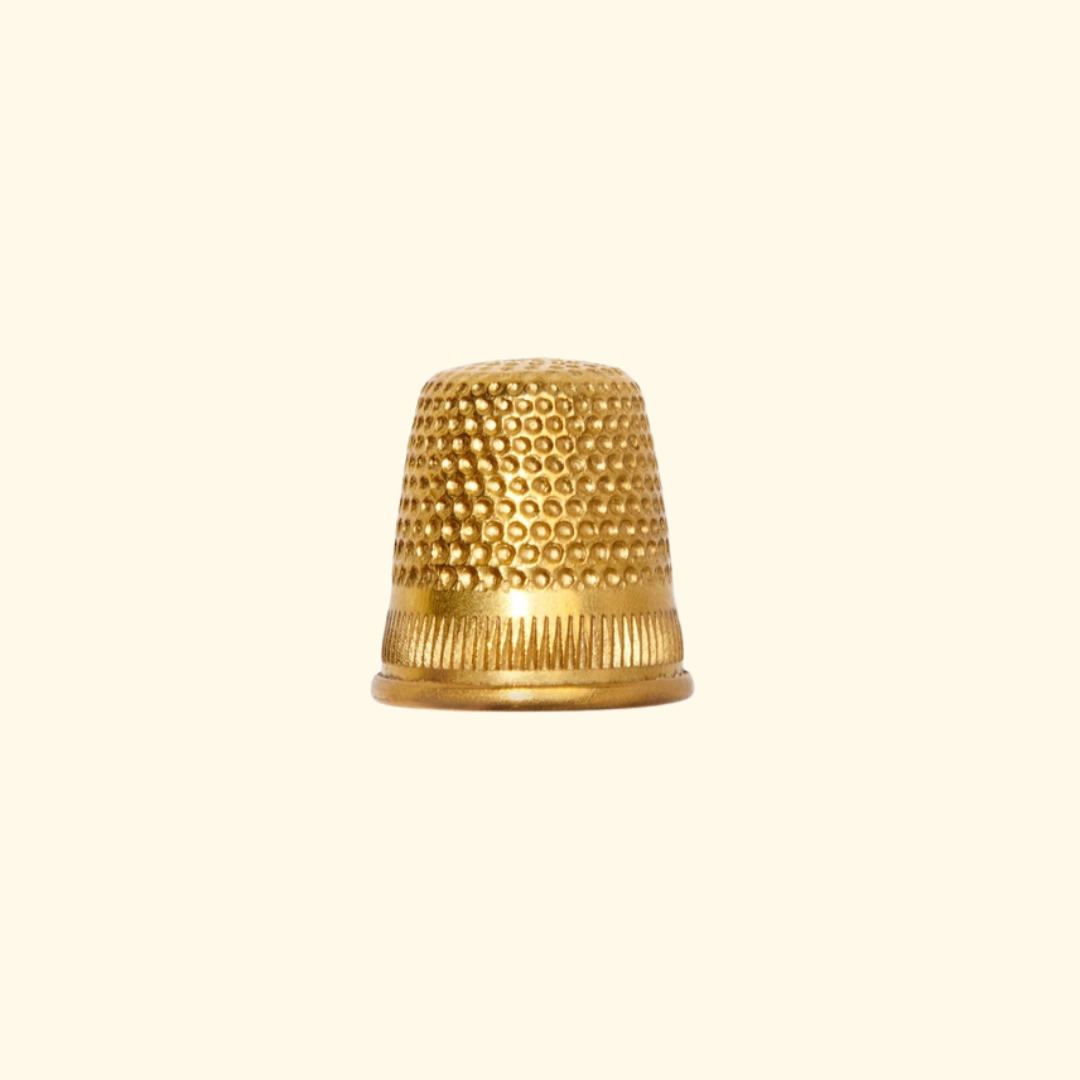 A small metallic gold thimble with a textured beaded top and ribbed base, centered on a plain cream background.