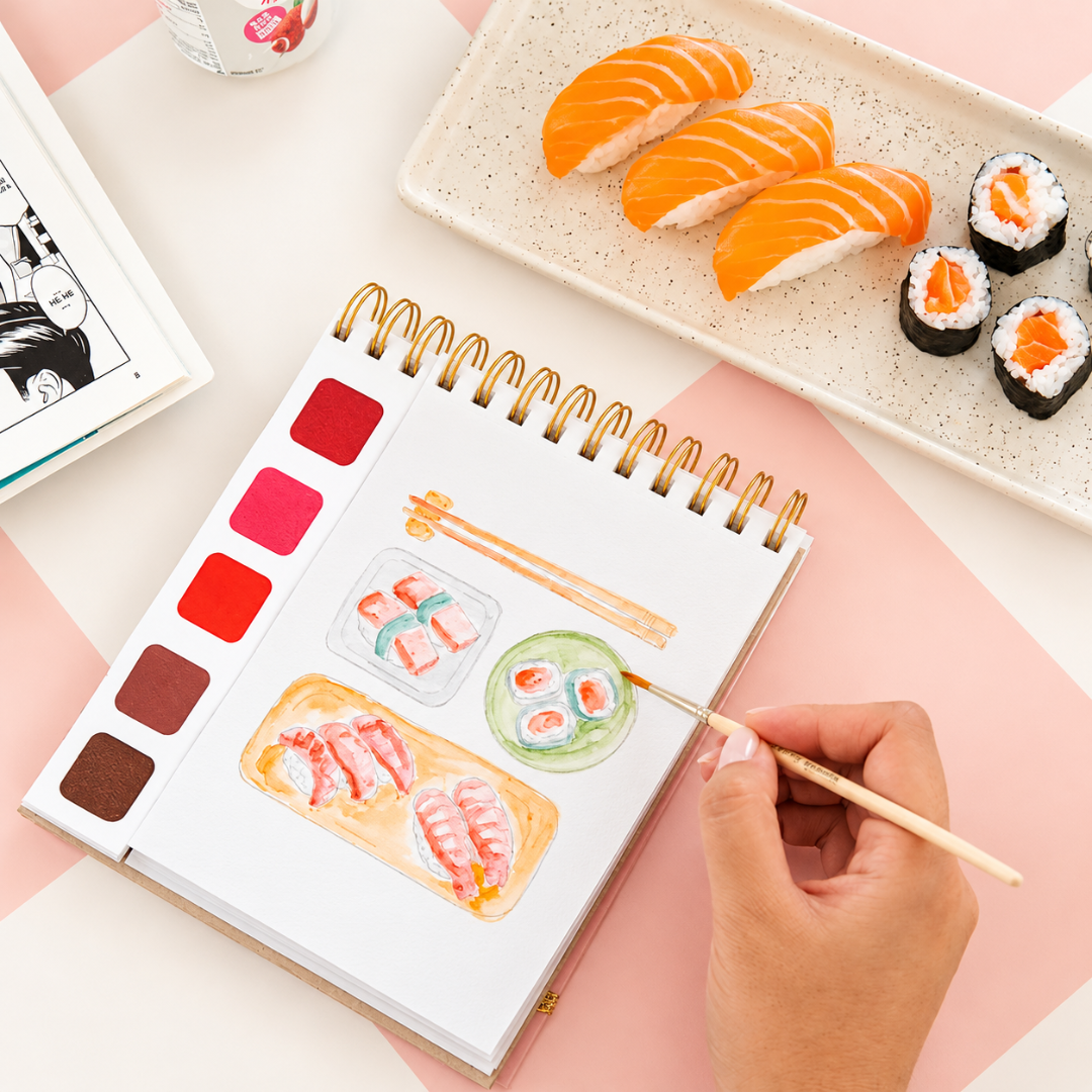 Close-up of the Japan Watercolour Travel Book by La Petite Epicerie being painted with a fine brush, featuring colourful sushi illustrations and a built-in watercolour palette.