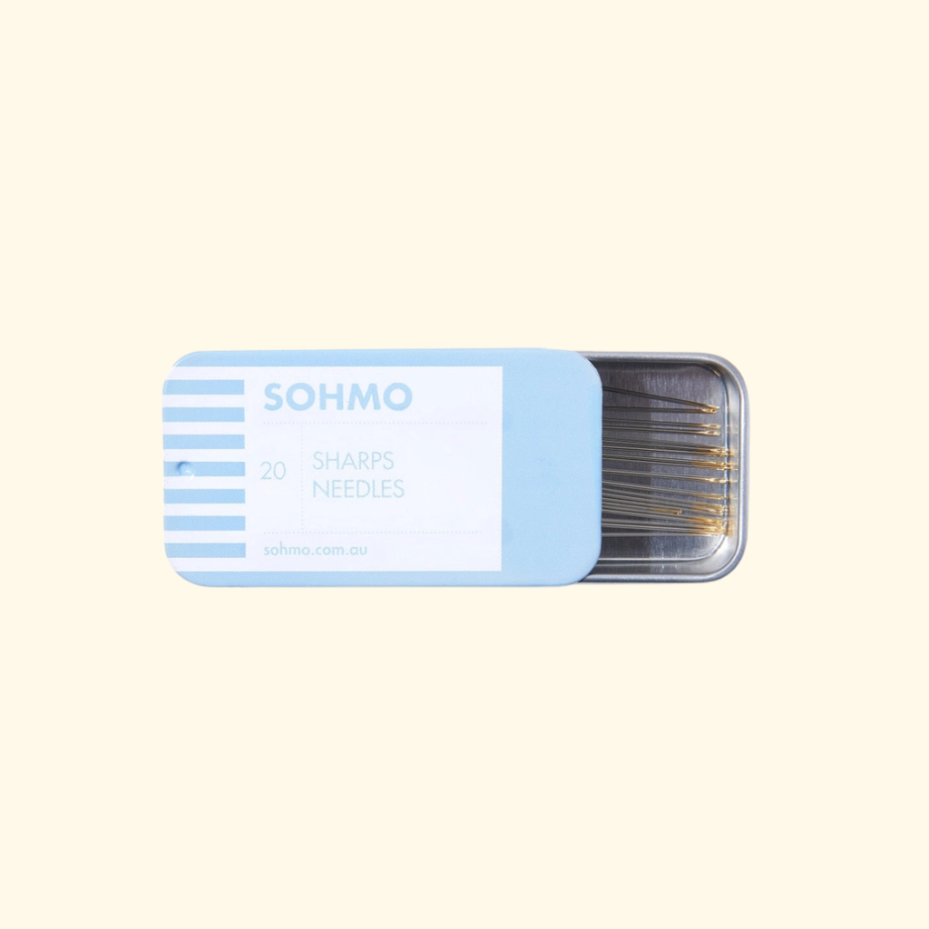 A light blue metal tin of SOHMO brand 20 sharps needles, partially open to reveal the needles inside, set against a solid pale cream background.