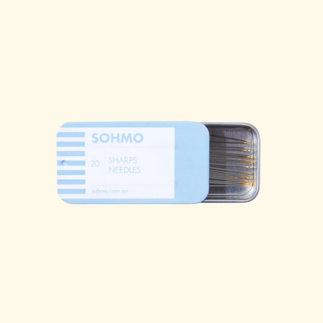 A light blue metal tin of SOHMO brand 20 sharps needles, partially open to reveal the needles inside, set against a solid pale cream background.