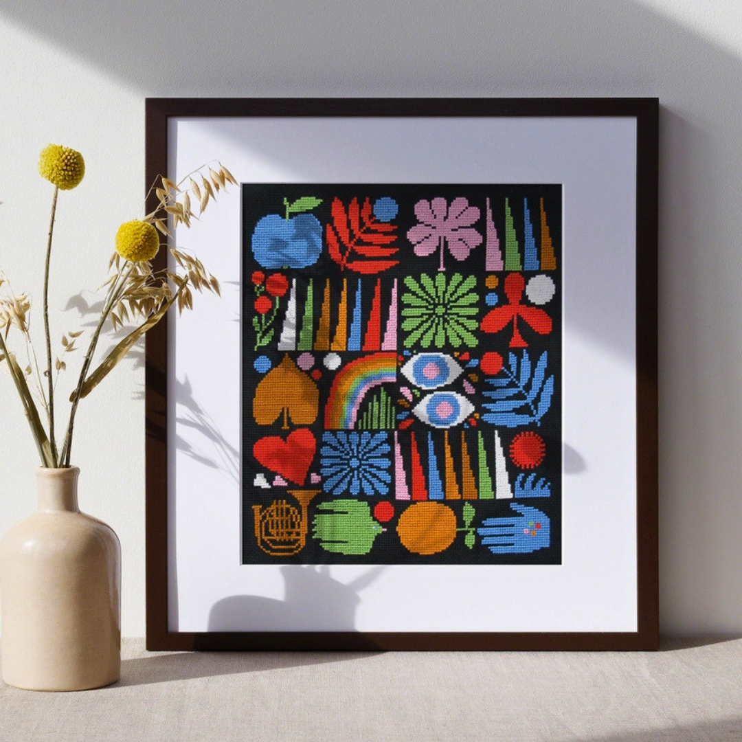 Framed Joyful Grid cross stitch displayed on a shelf with dried flowers in a modern home setting.