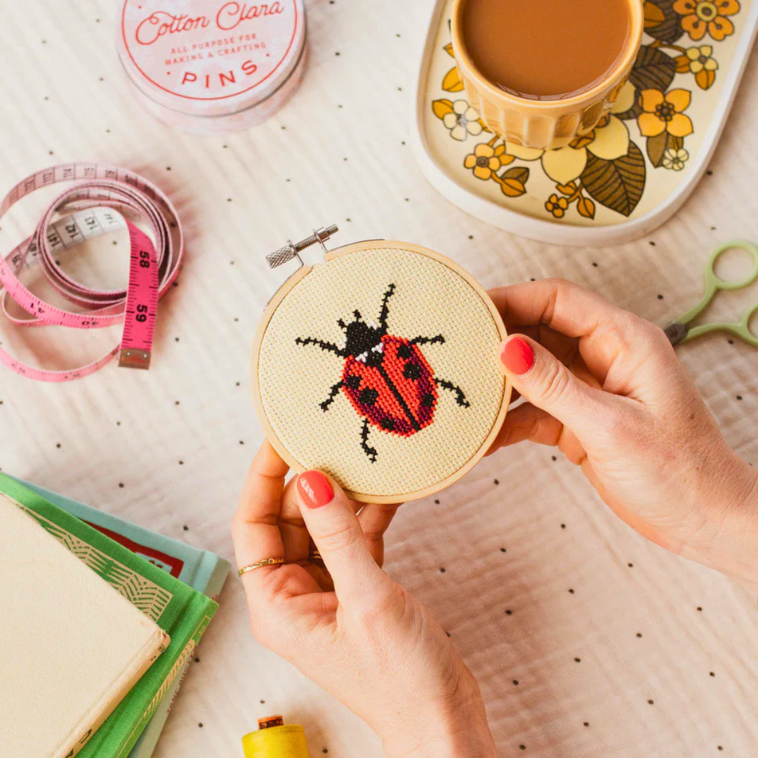 Hands stitching the ladybird cross stitch design using the Cotton Clara craft kit.