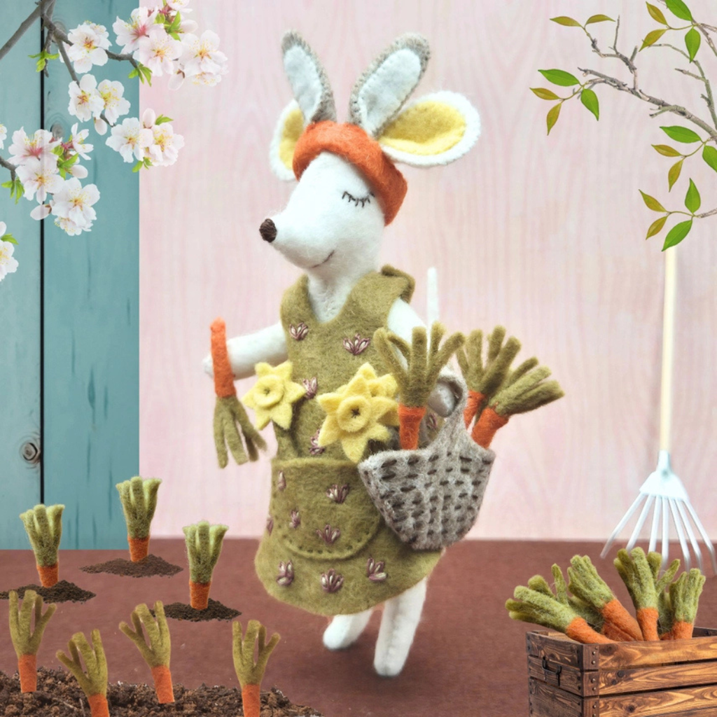 Handmade felt gardener mouse carrying a basket of vegetables, styled among plants and flowers.
