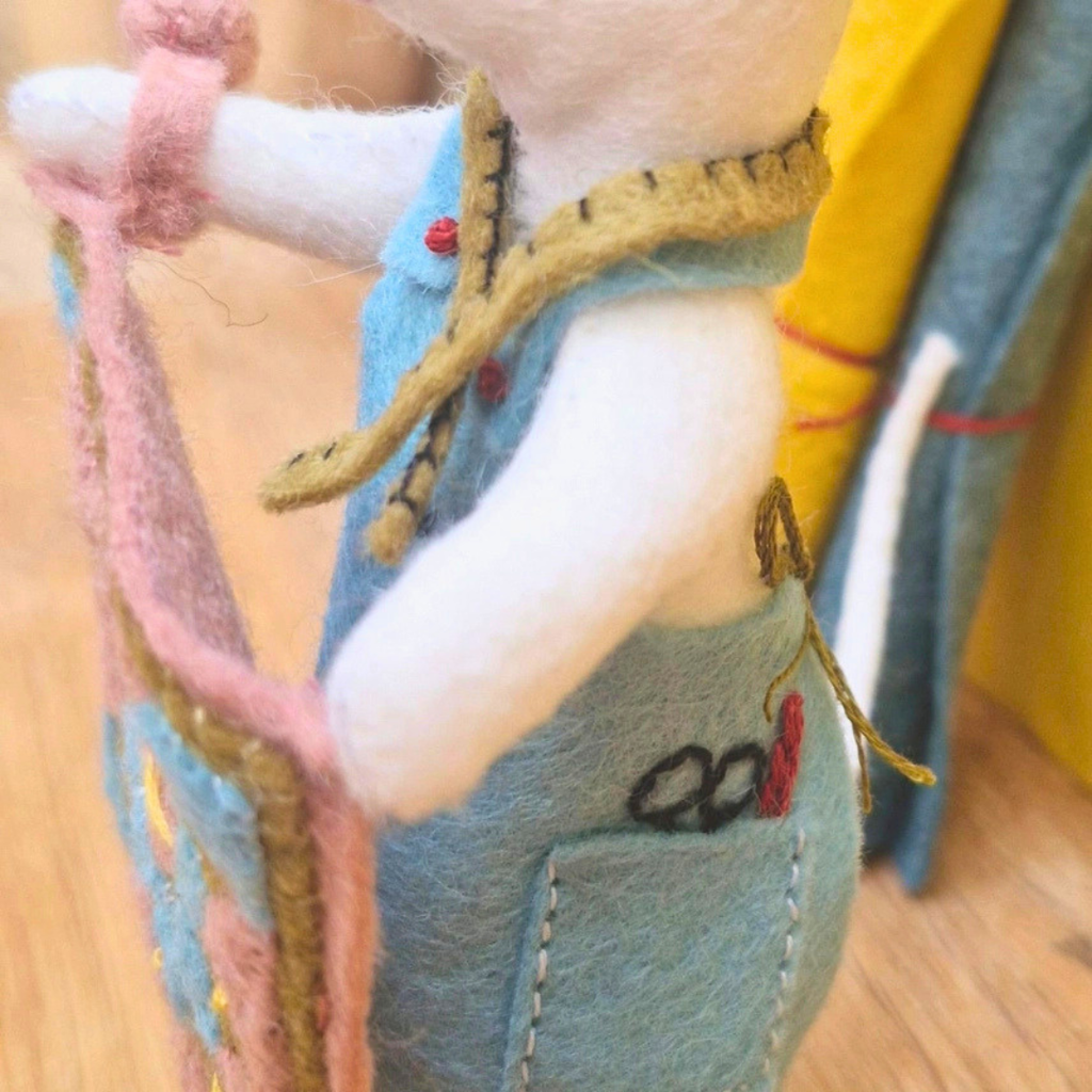 Close-up of the felt mouse holding her miniature patchwork quilt, with embroidered sewing scissors on her apron.