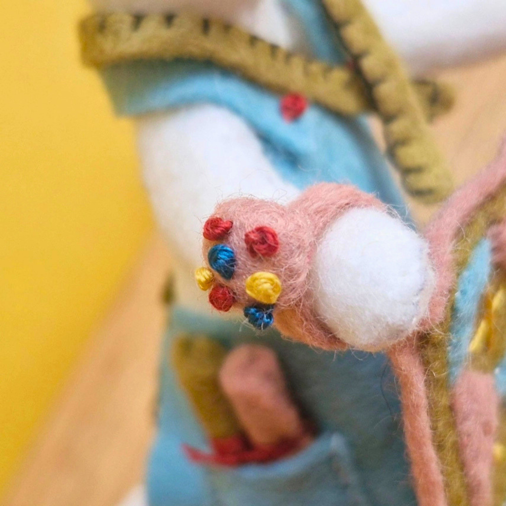 Close-up of the mouse carrying a miniature felt pincushion decorated with colourful pins.