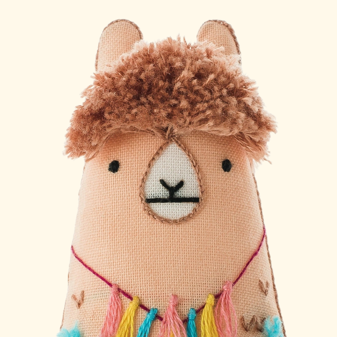 Close-up of the finished llama embroidery doll featuring a stitched face, textured fringe and colourful tassels.