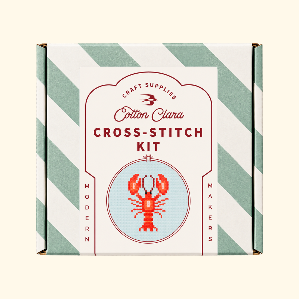 Cotton Clara Lobster Cross Stitch Kit in its mint green and white striped presentation box.