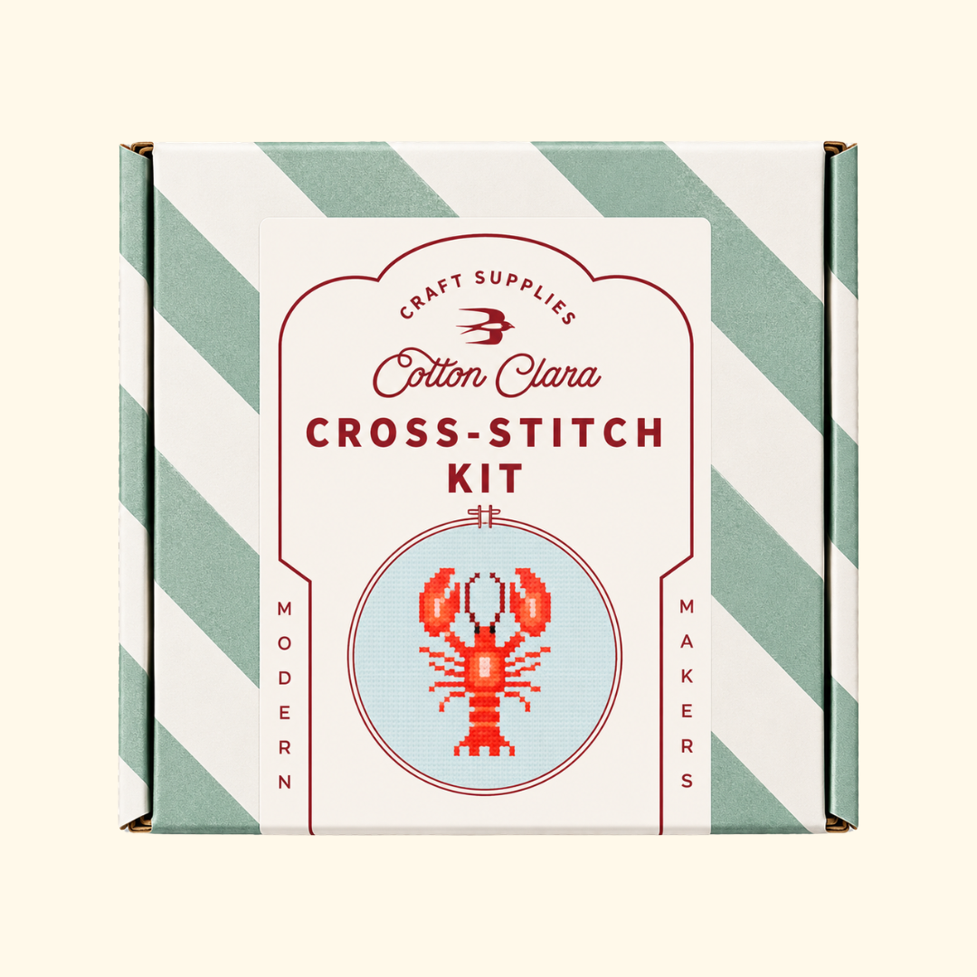 Cotton Clara Lobster Cross Stitch Kit in its mint green and white striped presentation box.