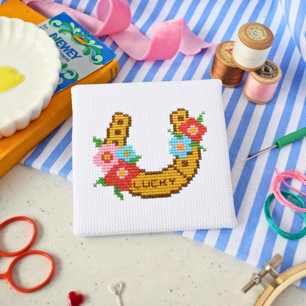Finished Lucky Horseshoe Mini Cross Stitch Kit displayed with embroidery scissors, thread and colourful craft supplies.