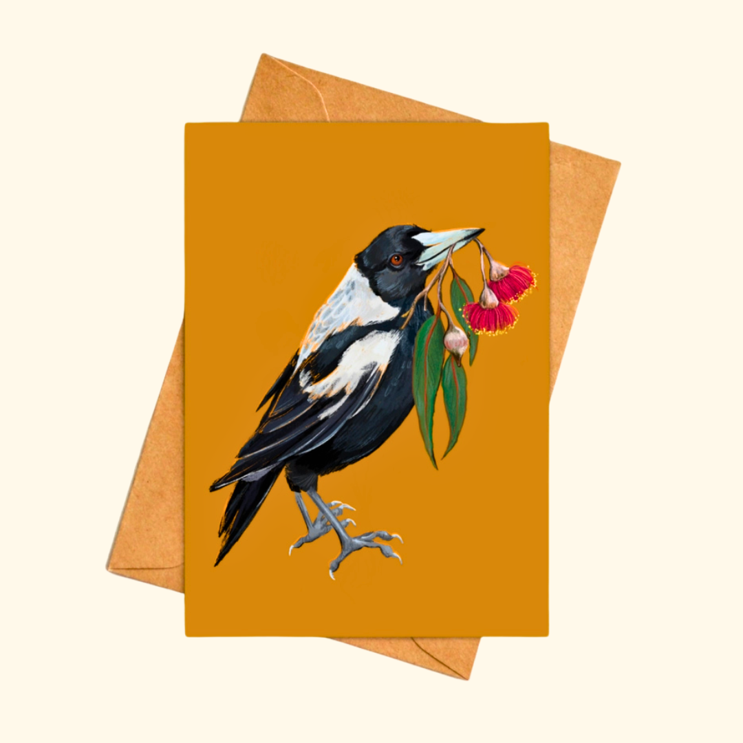 Magic Magpie greeting card shown with a matching kraft envelope, featuring an illustrated Australian magpie carrying a sprig of red gum blossoms.
