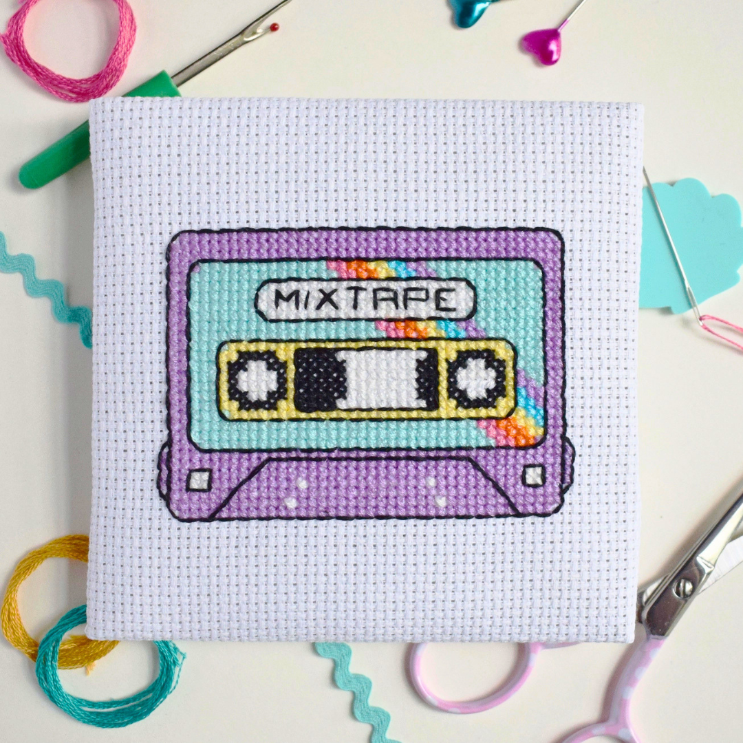 Mixtape cassette cross stitch design surrounded by scissors, thread, a needle and colourful paper.