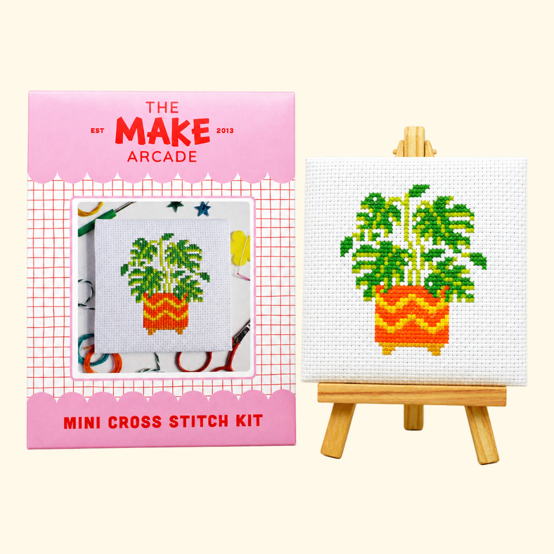 The Make Arcade Monstera Mini Cross Stitch Kit beside the completed design on a miniature easel.