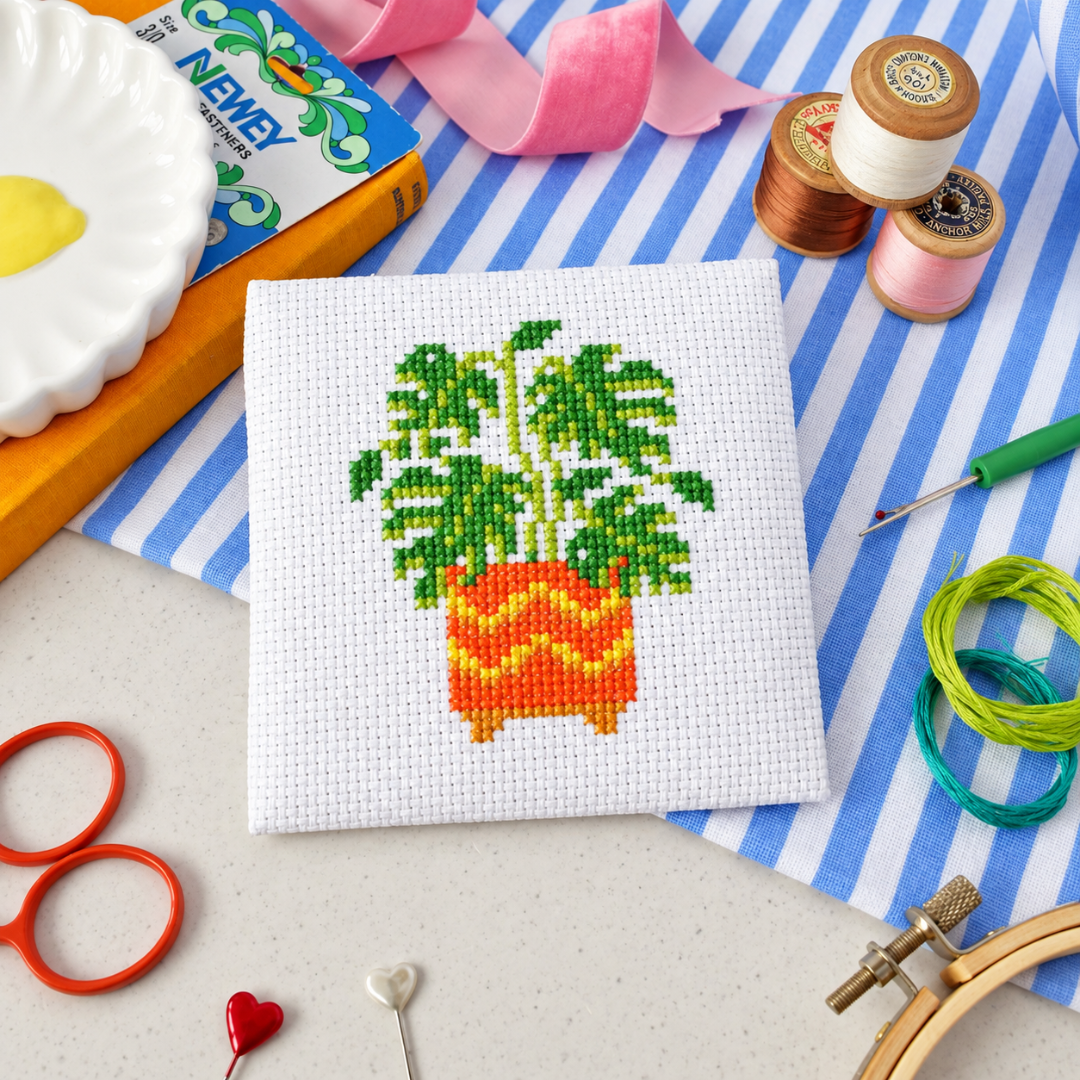 Monstera plant cross stitch design surrounded by scissors, thread, stars and a yellow flower.