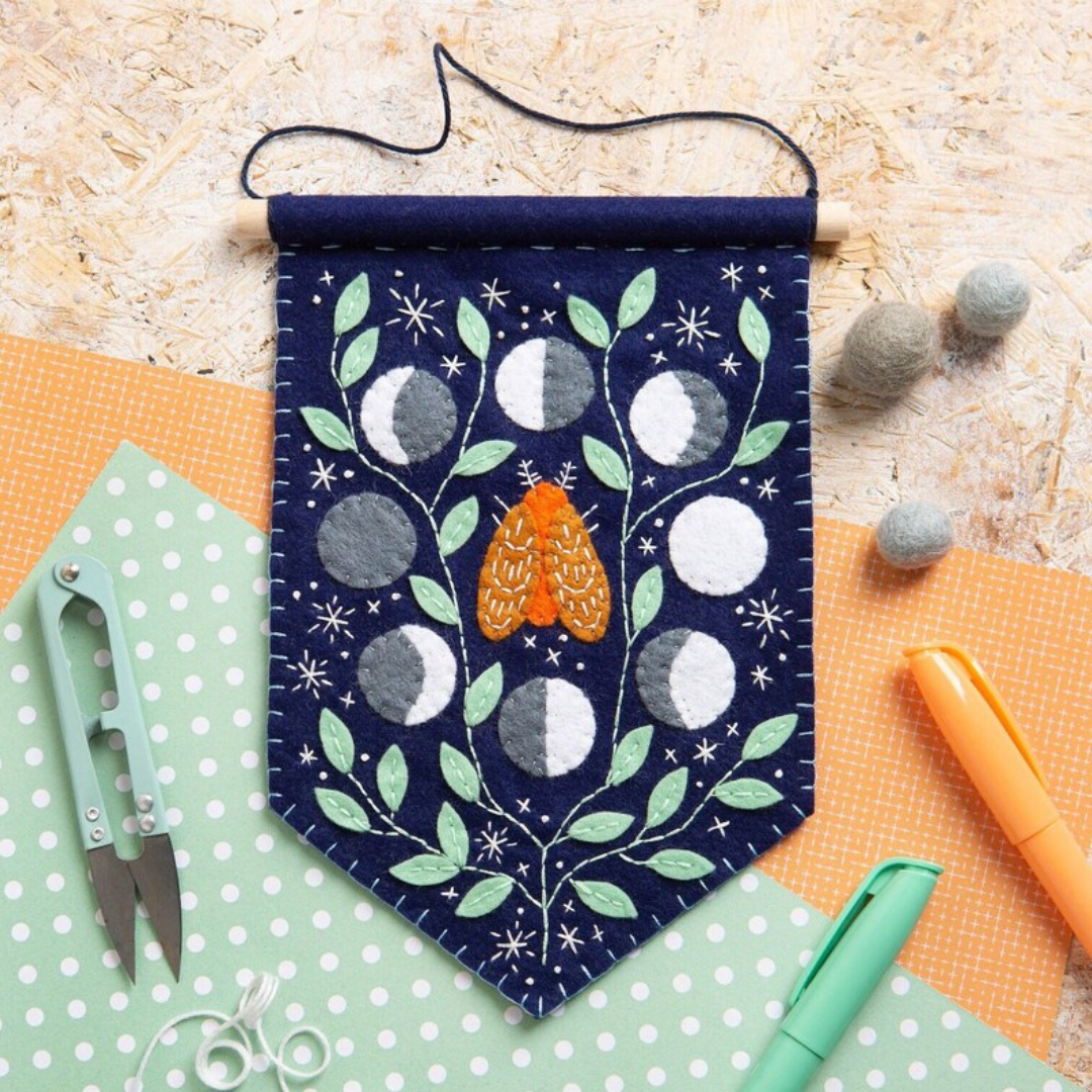 Completed Moonlight felt wall hanging displayed with scissors, thread and craft materials on a work surface