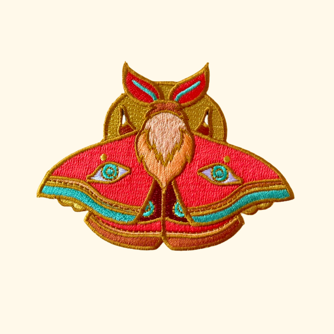 Colourful moth embroidered iron on patch by Ashlea Bechaz Illustration featuring outstretched wings, intricate red, green and gold stitching and decorative patterns on a cream background.