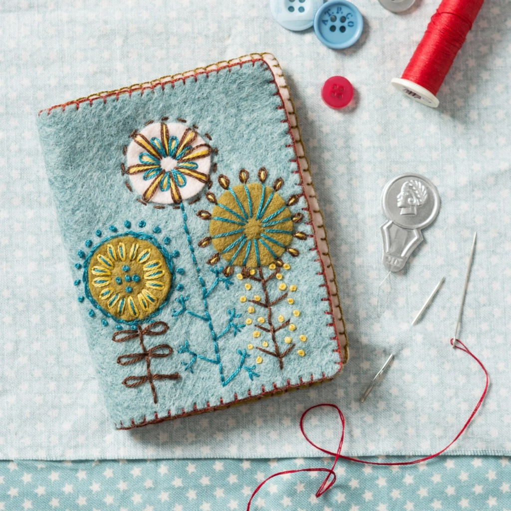 Completed embroidered felt needle case displayed with buttons, thread, needle and sewing accessories.