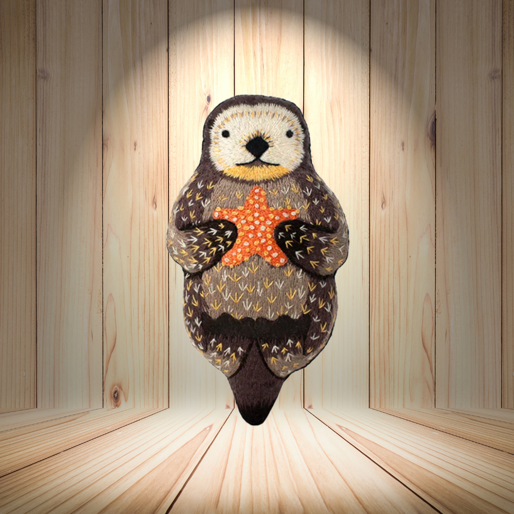 Finished otter embroidery kit displayed in a wooden setting