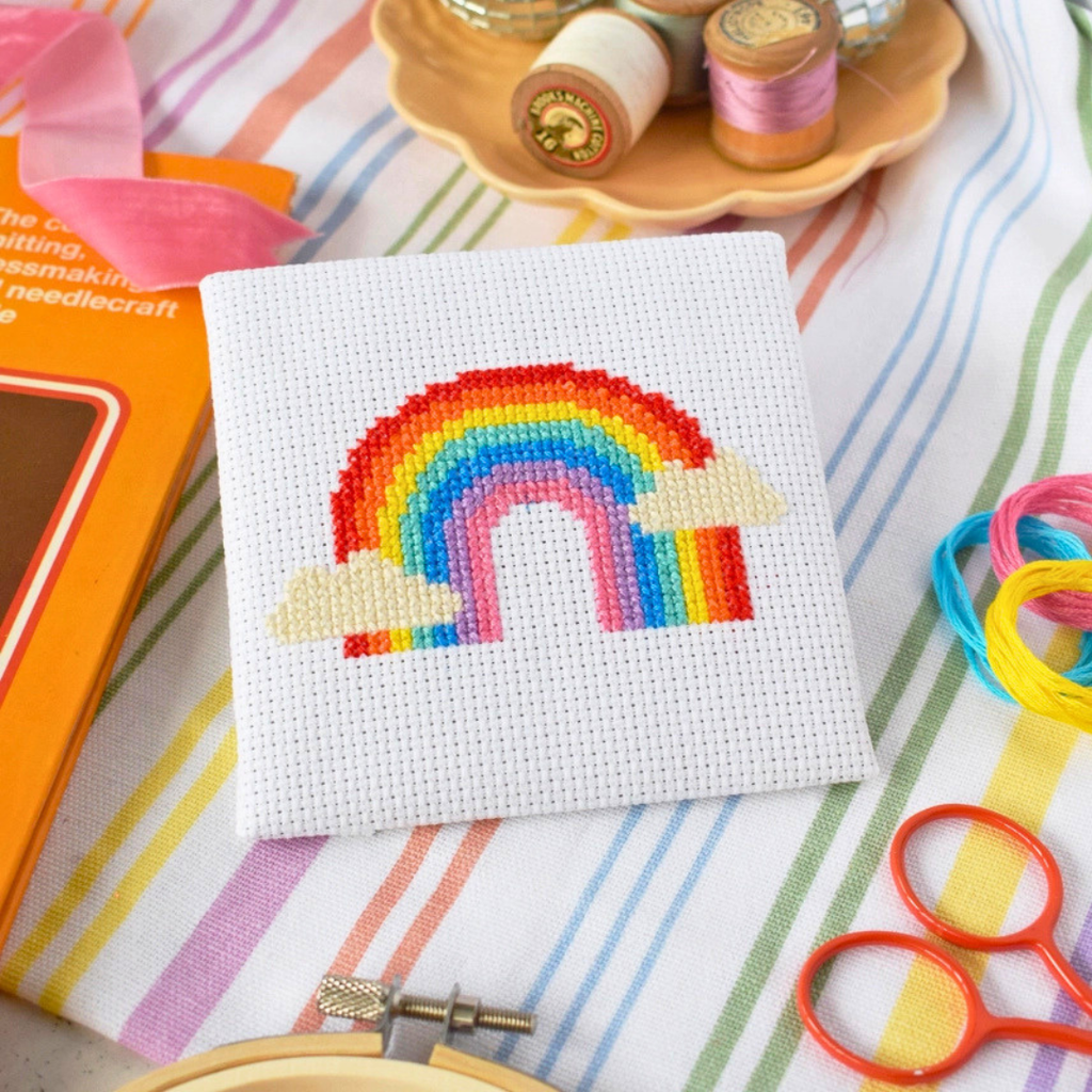 Finished Over The Rainbow Mini Cross Stitch Kit displayed with embroidery scissors, thread and colourful craft supplies.