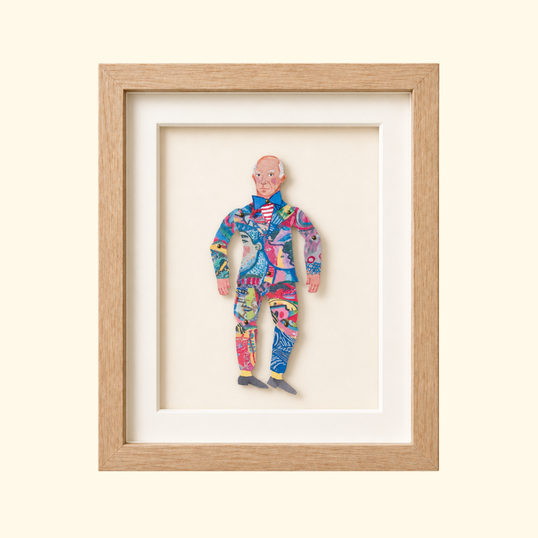 Framed Pablo Picasso paper puppet wearing a brightly patterned suit and striped shirt.