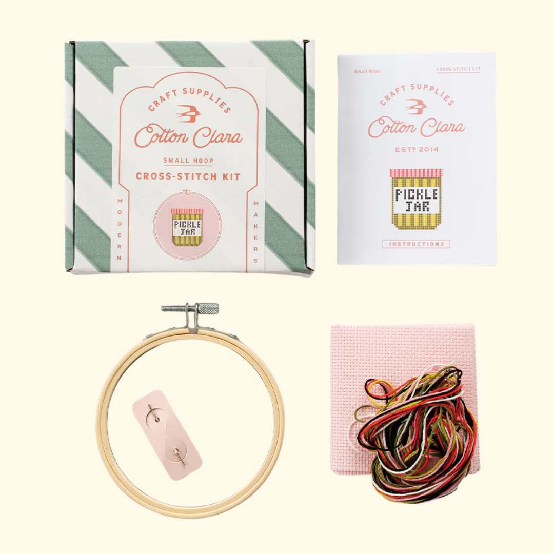 Contents of the Cotton Clara Pickle Jar Cross Stitch Kit including hoop, Aida fabric, threads, needle and instructions.