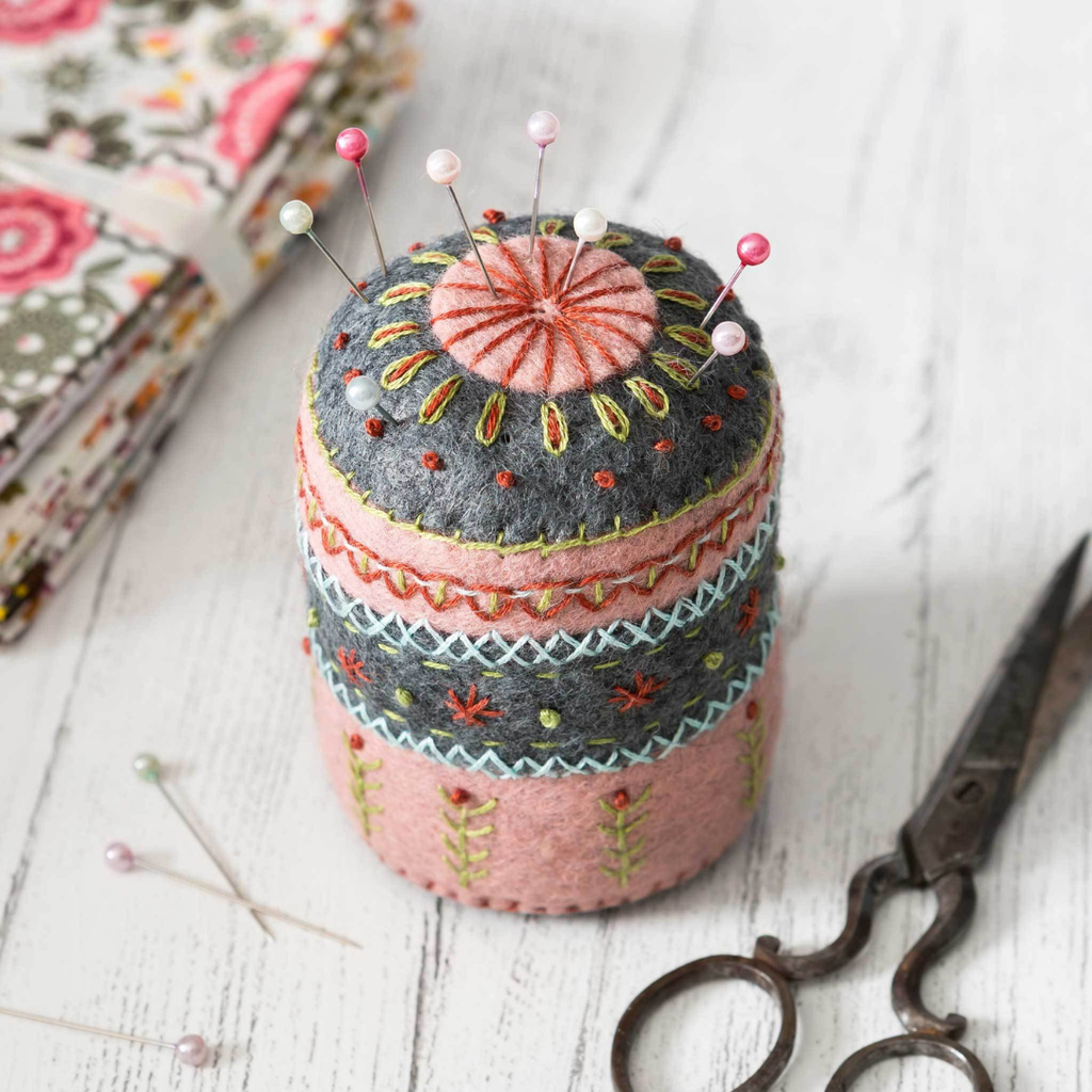 Finished embroidered felt pincushion displayed beside sewing scissors and floral fabric