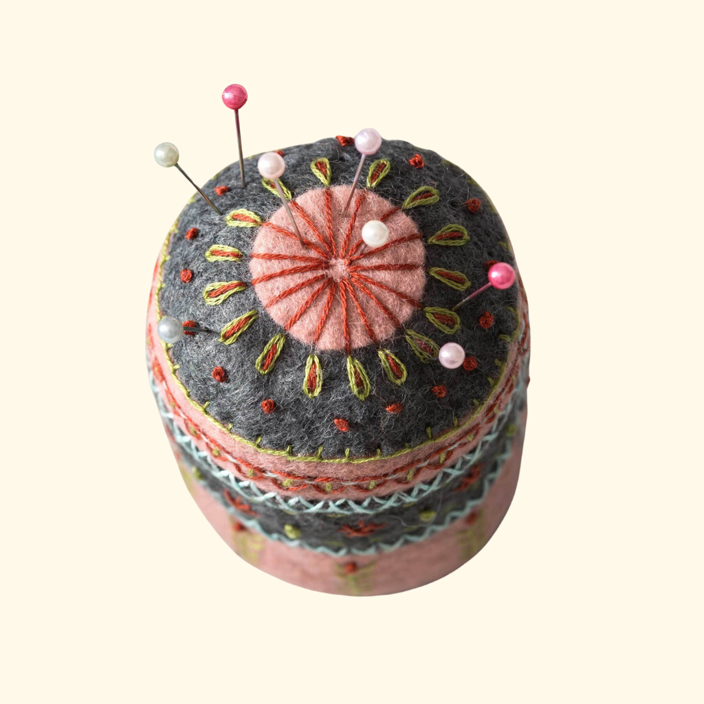 Top view of embroidered felt pincushion showing decorative stitching, button centre and colourful pins