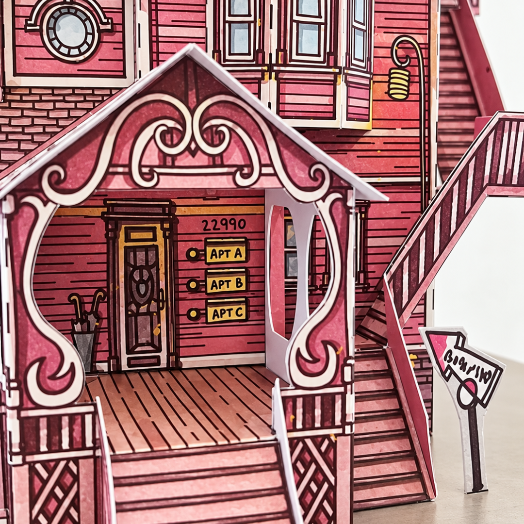 Close-up of Coraline's Pink Palace Apartments paper model showing the ornate front entrance, pink timber cladding, windows and architectural details.