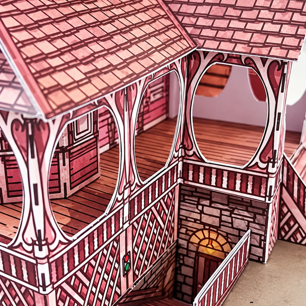 Side view of the assembled Pink Palace Apartments paper model kit showing the intricate roof tiles, timber framework, balconies and exterior staircases.