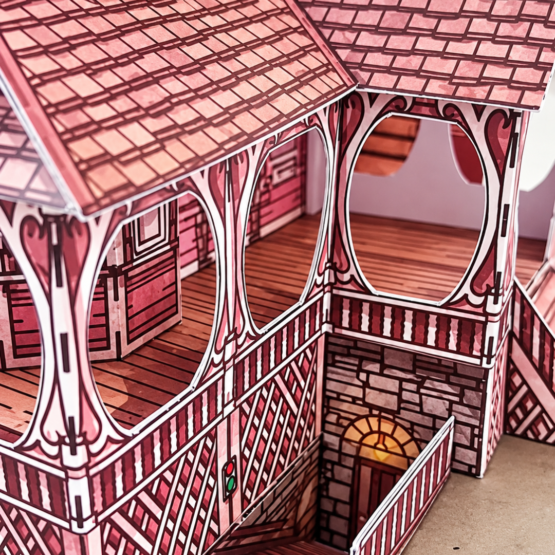 Side view of the assembled Pink Palace Apartments paper model kit showing the intricate roof tiles, timber framework, balconies and exterior staircases.