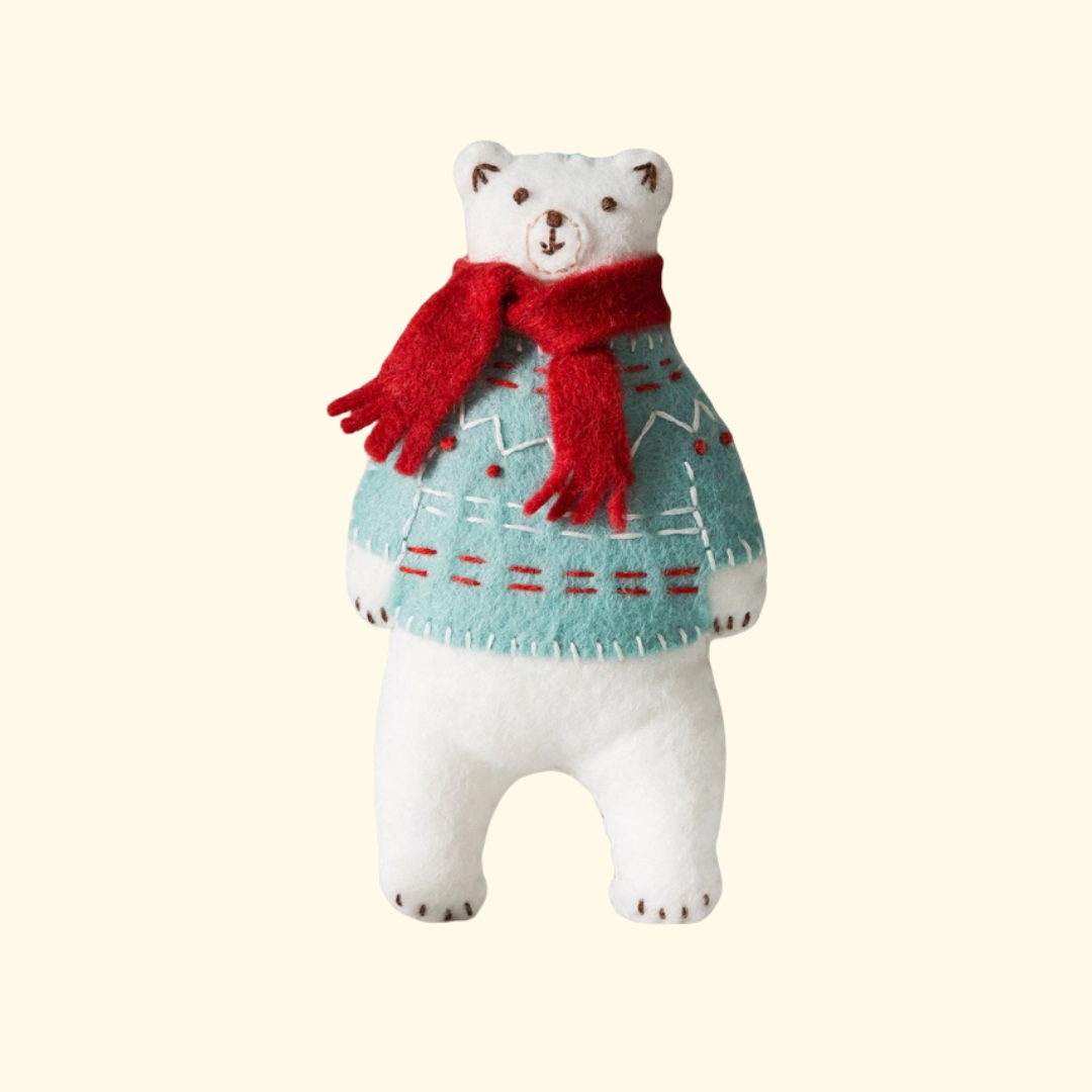Completed polar bear felt craft figure wearing a red scarf, patterned jumper and red boots on a plain background.